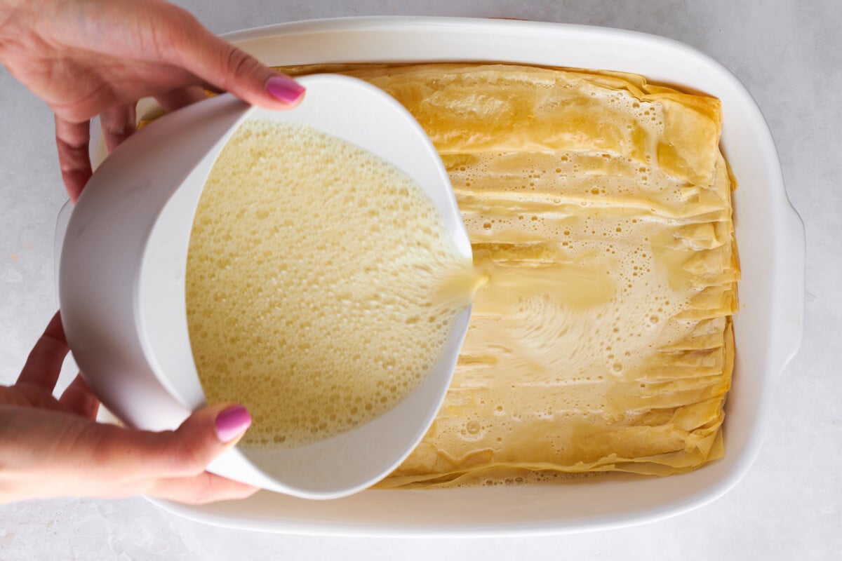 Egg mixture being poured over baked crinkled phyllo.