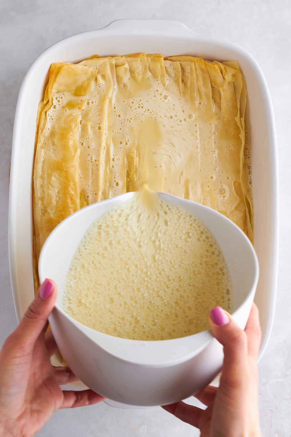 Egg mixture being poured over phyllo dough in a baking dish. 