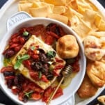 A baking dish of Mediterranean baked feta dip surrounded by pita chips and puffs.