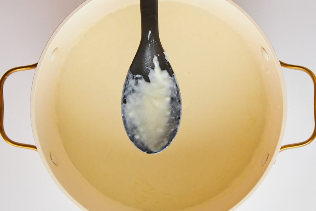 A spoon over a pot of bechamel sauce.