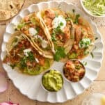 A plate of four salmon tacos with guacamole and pico de gallo.