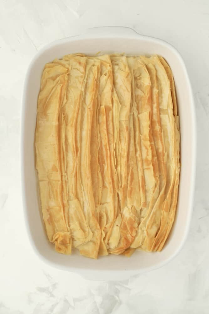 cooked, flaky, golden-brown phyllo dough sheets folded on top of each other and placed in the bottom of a white baking dish