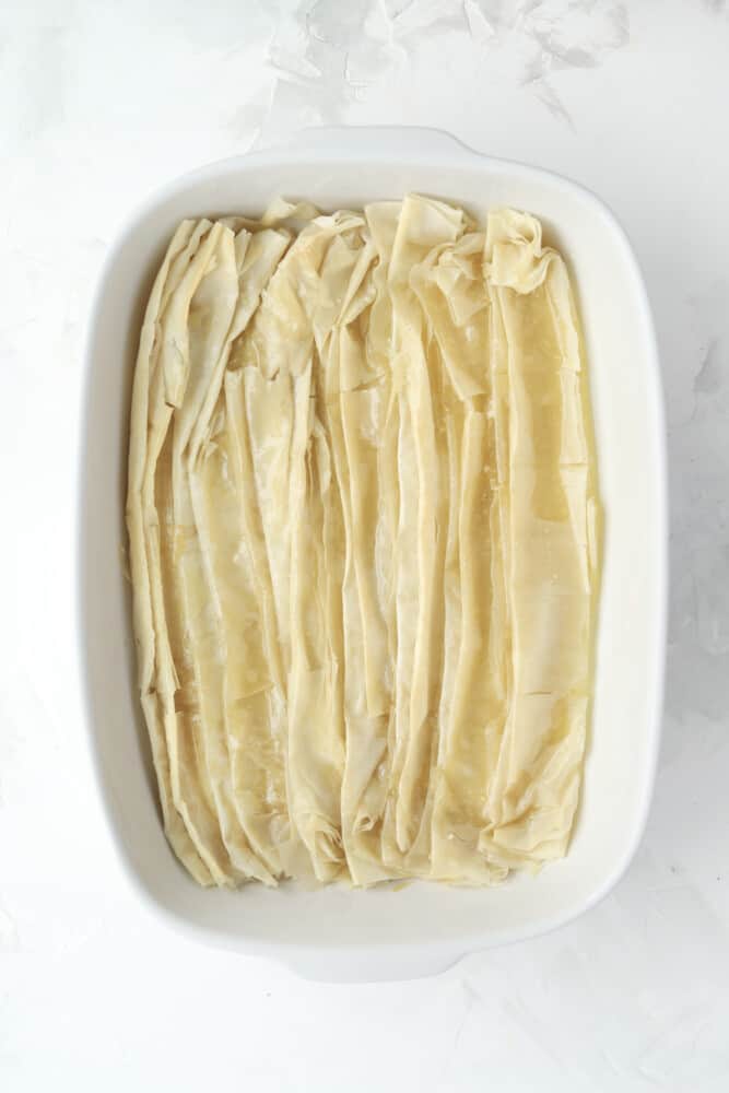 overhead image of uncooked phyllo dough sheets layered on top of each other and placed in the bottom of a baking dish