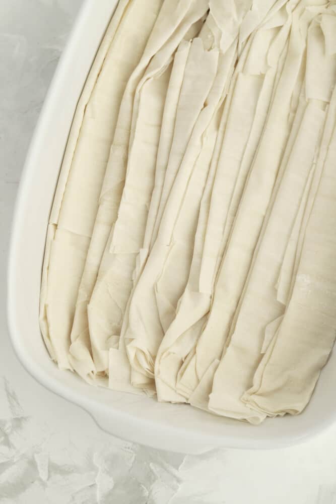 overhead image of folded phyllo dough layers placed in the bottom of a white baking dish