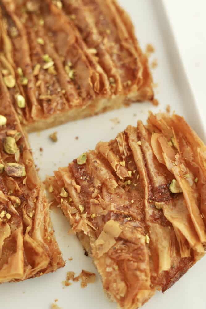 close up image of a square of baked crinkle phyllo dough topped with chopped pistachios cut away from the whole recipe