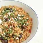 side view of a bowl of one pot Greek couscous topped with feta and fresh herbs