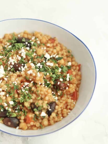 side view of a bowl of one pot Greek couscous topped with feta and fresh herbs