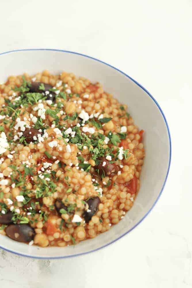 side view of a bowl of one pot Greek couscous topped with feta and fresh herbs