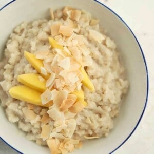 a bowl of slow cooker coconut sticky rice topped with mango slices and coconut flakes