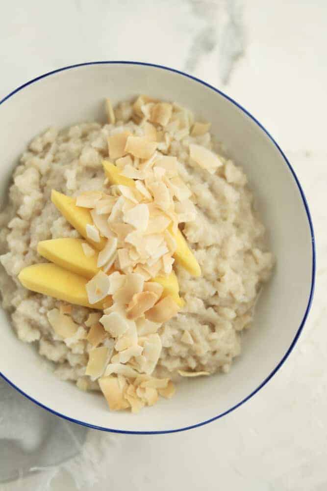 a bowl of slow cooker coconut sticky rice topped with mango slices and coconut flakes
