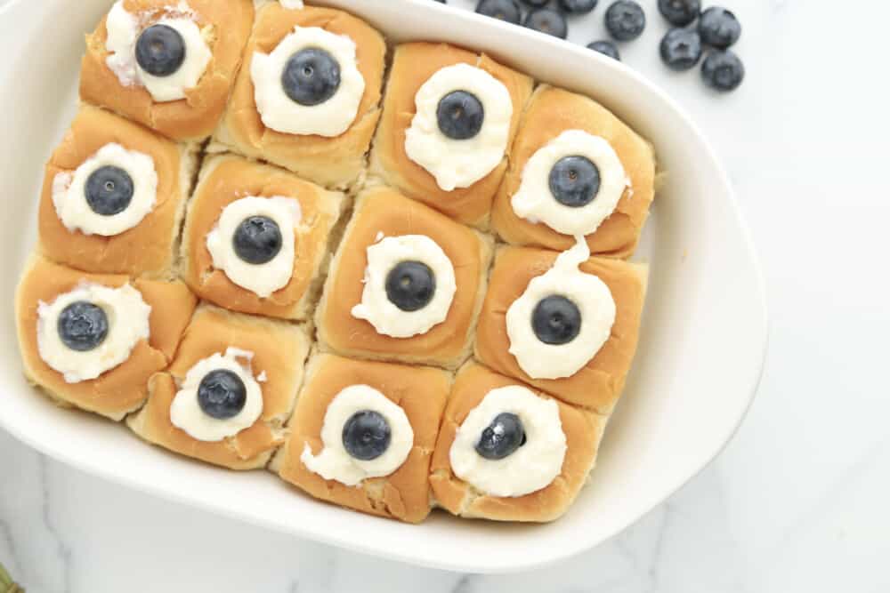 overhead image of Hawaiian roll lemon blueberry french toast with ricotta in a white baking dish with blueberries off to the side
