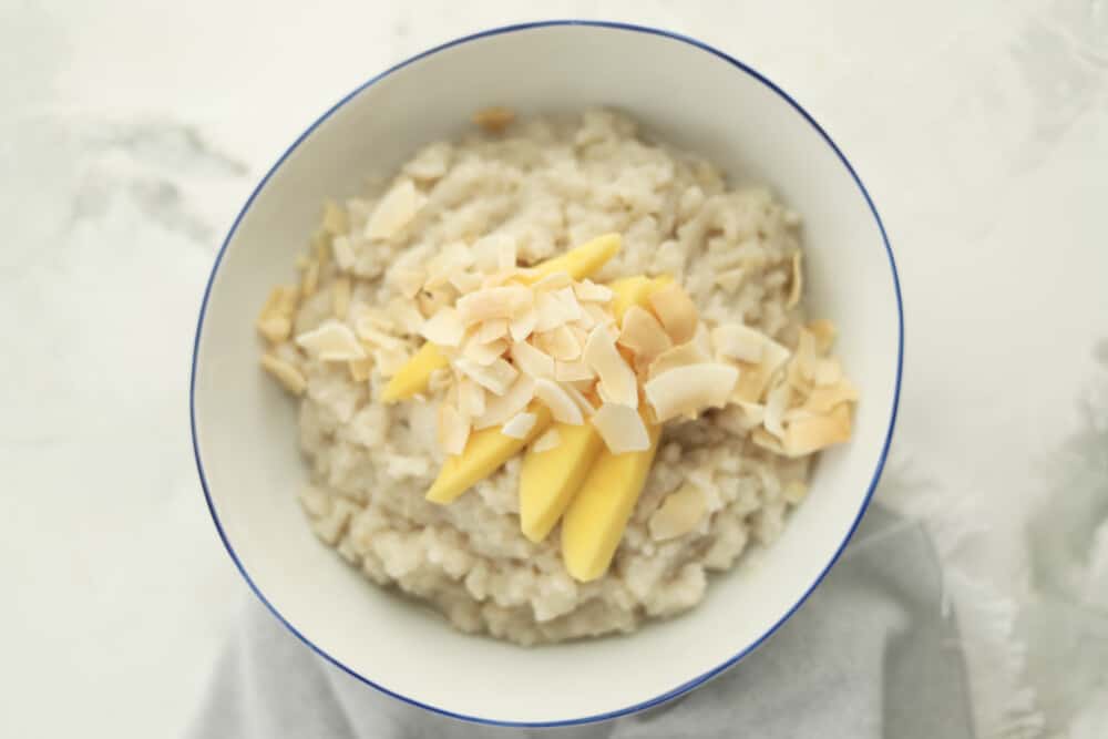 a bowl of slow cooker coconut sticky rice topped with sliced mangoes and coconut flakes 