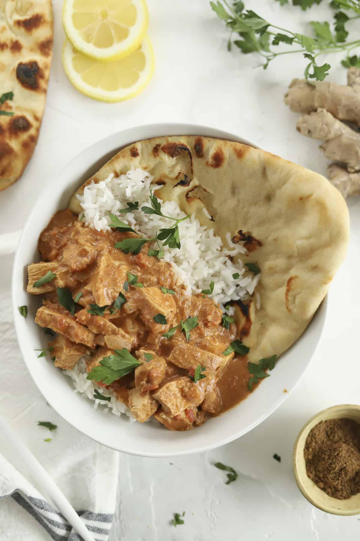 a bowl of chicken tikka masala over a bed of white rice with naan on the side.