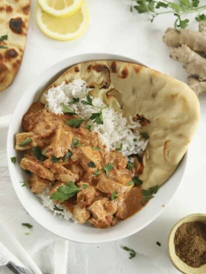 a bowl of chicken tikka masala over a bed of rice with naan on the side.