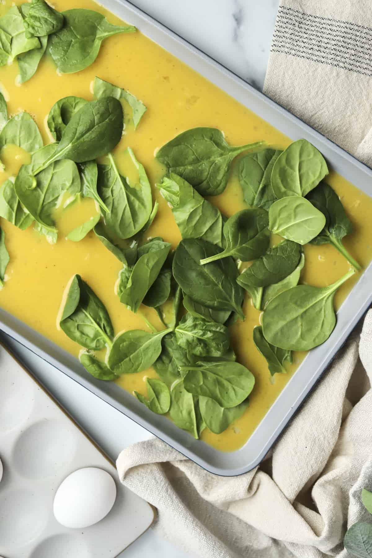 raw eggs topped with spinach in a pan