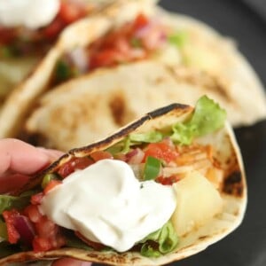 a hand holding a crock pot chicken fajita taco topped with sour cream