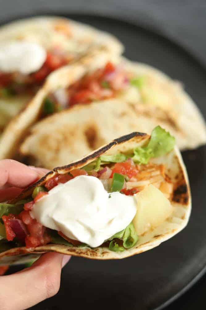 a hand holding a crock pot chicken fajita taco topped with sour cream