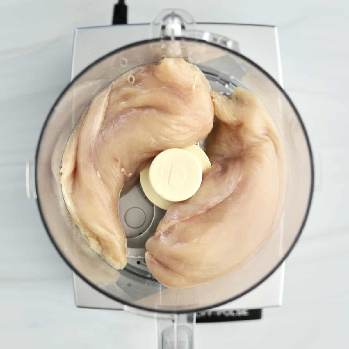 overhead image of raw chicken breasts in a food processor