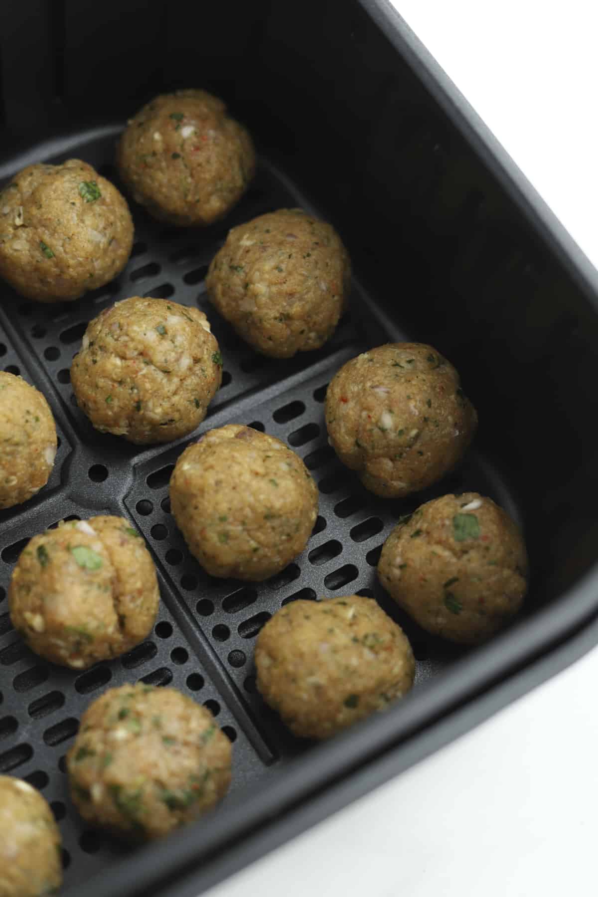 Raw chicken kofta meatballs in an air fryer basket. 