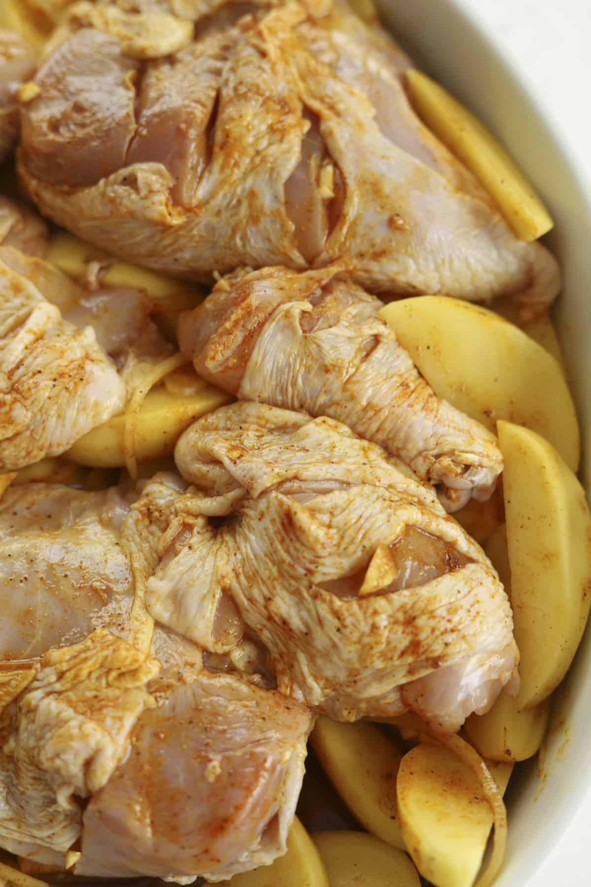 raw seasoned potatoes, onions, and chicken in a baking dish