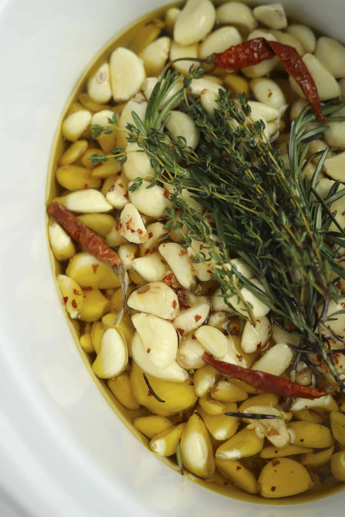 closeup overhead slow cooker garlic confit with fresh herbs
