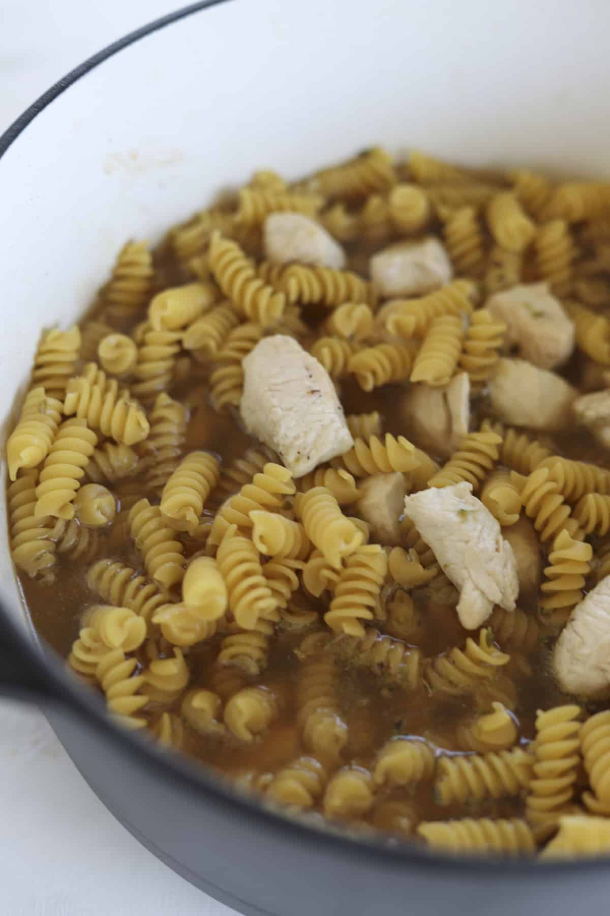 cooked chicken pieces, rotini noodles, and broth in a pot 