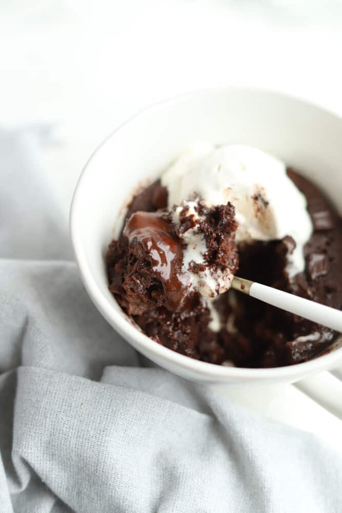 chocolate coffee mug cake topped with vanilla ice cream with a bite being lifted up with a spoon.