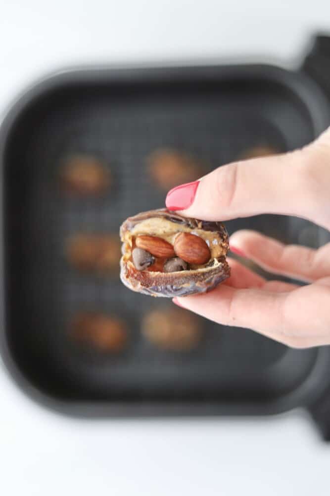 two fingers holding a date stuffed with nut butter, almonds, and chocolate chips