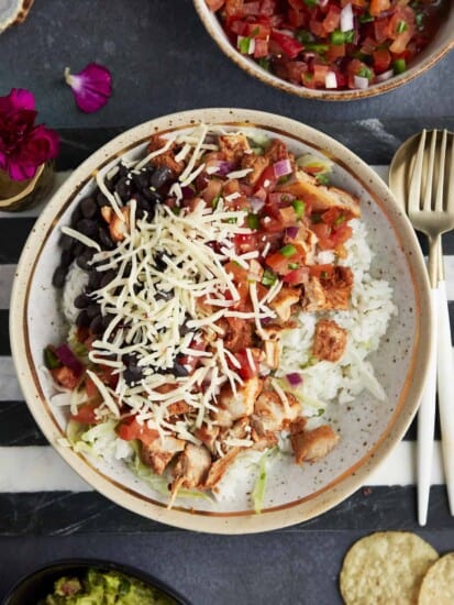 a homemade chipotle bowl with rice, chicken, lettuce, salsa, black beans, and cheese