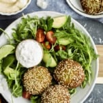a salad topped with three falafel balls and a bowl of tzatziki