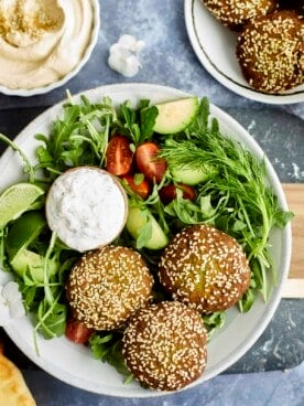 a salad topped with three falafel balls and a bowl of tzatziki