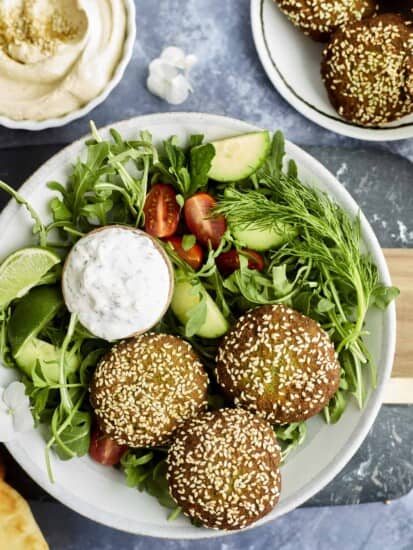 a salad topped with three falafel balls and a bowl of tzatziki