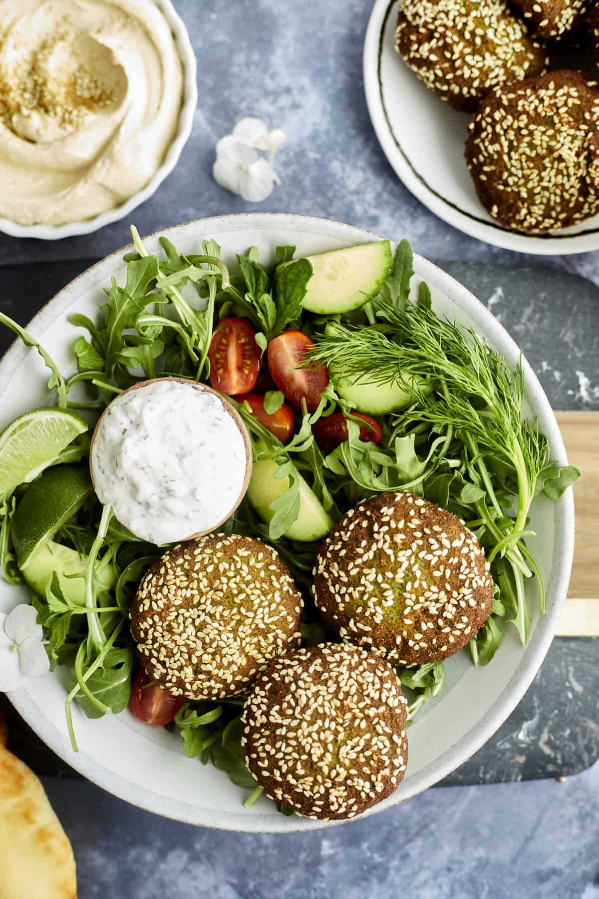 three pieces of falafel over a salad with a small bowl of tzatziki