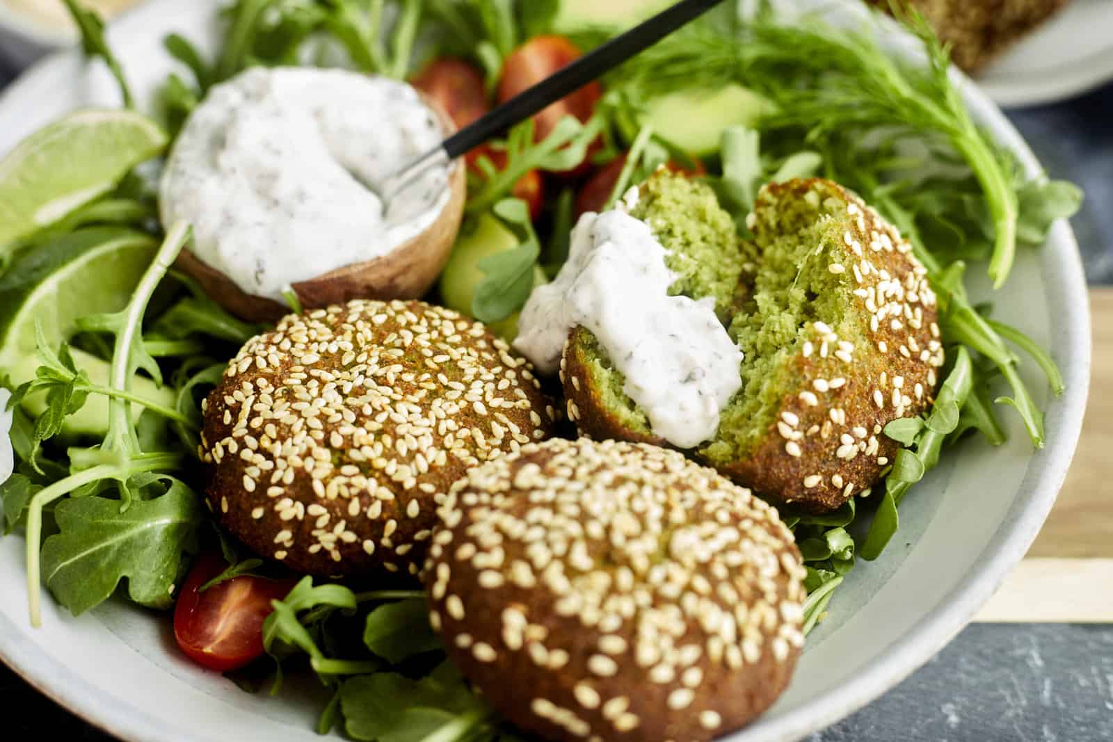 a salad with a small bowl of tzatziki and two whole falafel balls and a third split in half 