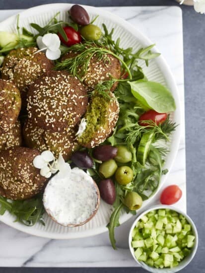 a plate of air fryer falafel over a bed of greens with a side of tzatziki