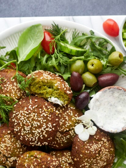 a plate of air fryer falafel over a bed of greens with a side of tzatziki.