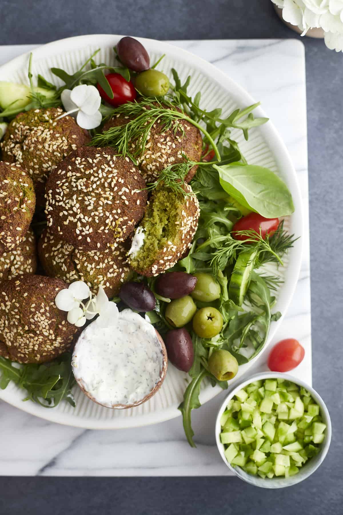 a plate o fair fryer falafel over a bed of greens with a side of tzatziki