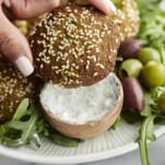 two fingers holding an air fryer falafel topped with sesame seeds.