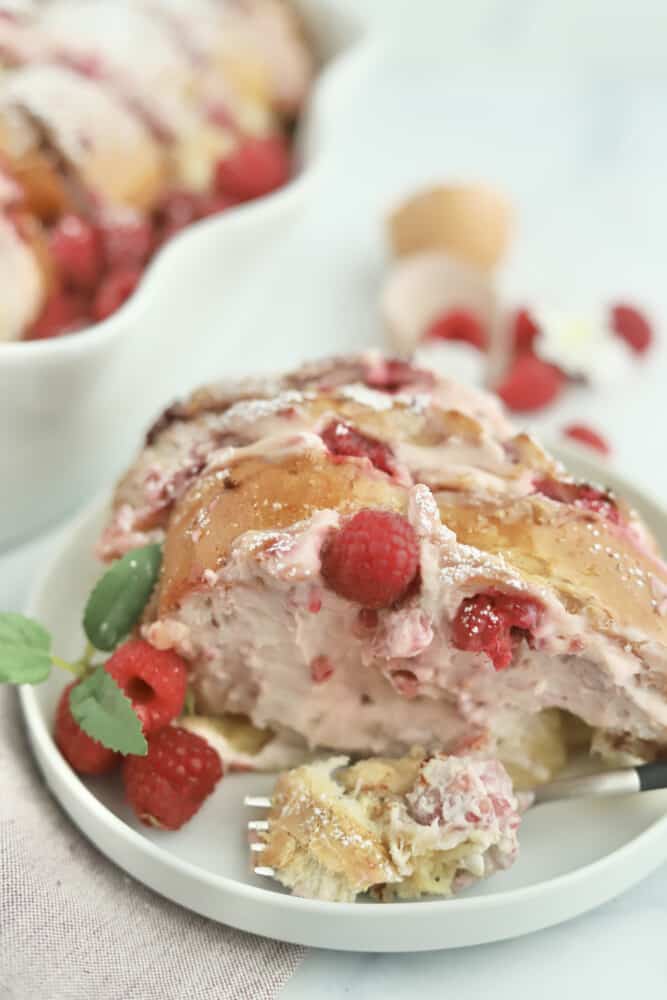a portion of raspberry cheesecake challah french toast on a white plate with fresh raspberries on the side