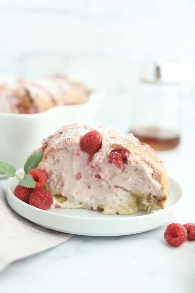 a side image of raspberry cheesecake challah french toast on a white plate topped with fresh strawberries