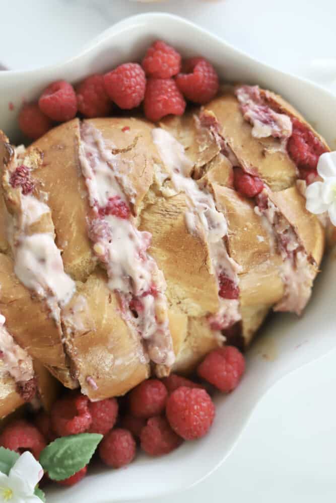 overhead image of raspberry cheesecake challah french toast in a white baking dish with fresh strawberries along the sides