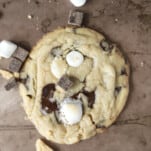 a single s'mores cookie with a few marshmallows, chocolate chunks, and graham crackers scattered around