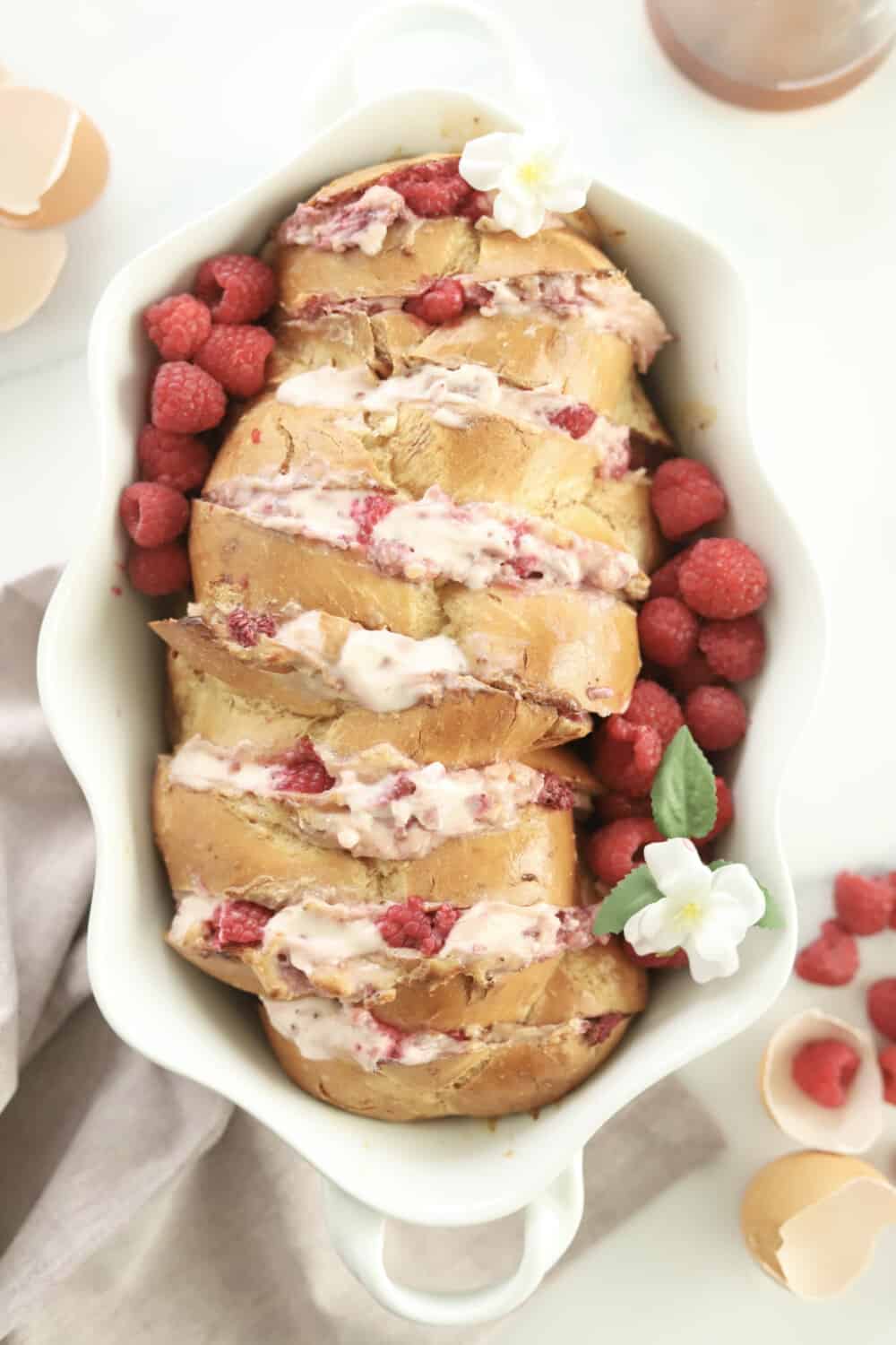 challah french toast cut hasselback and stuffed with raspberry cheesecake filling in a white baking dish with raspberries on the side