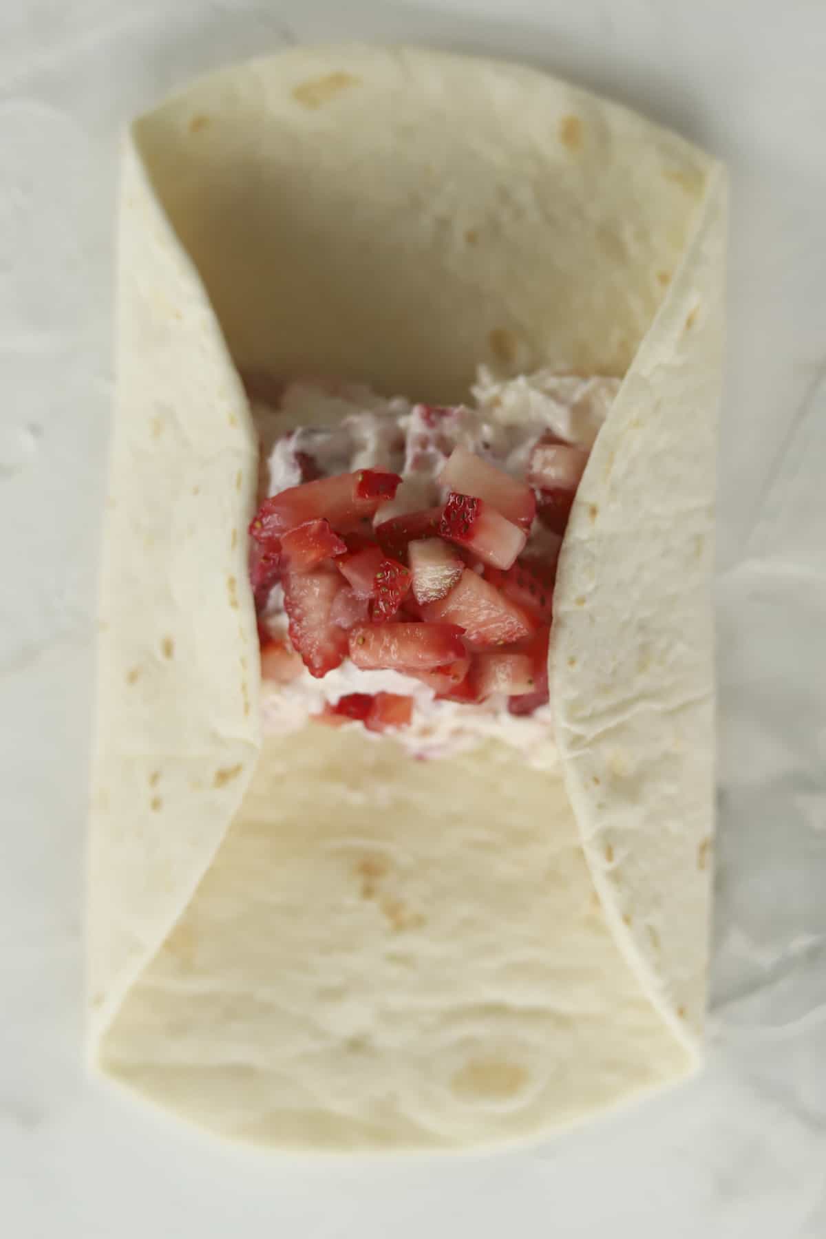 a tortilla being folded with a strawberry cheesecake filling
