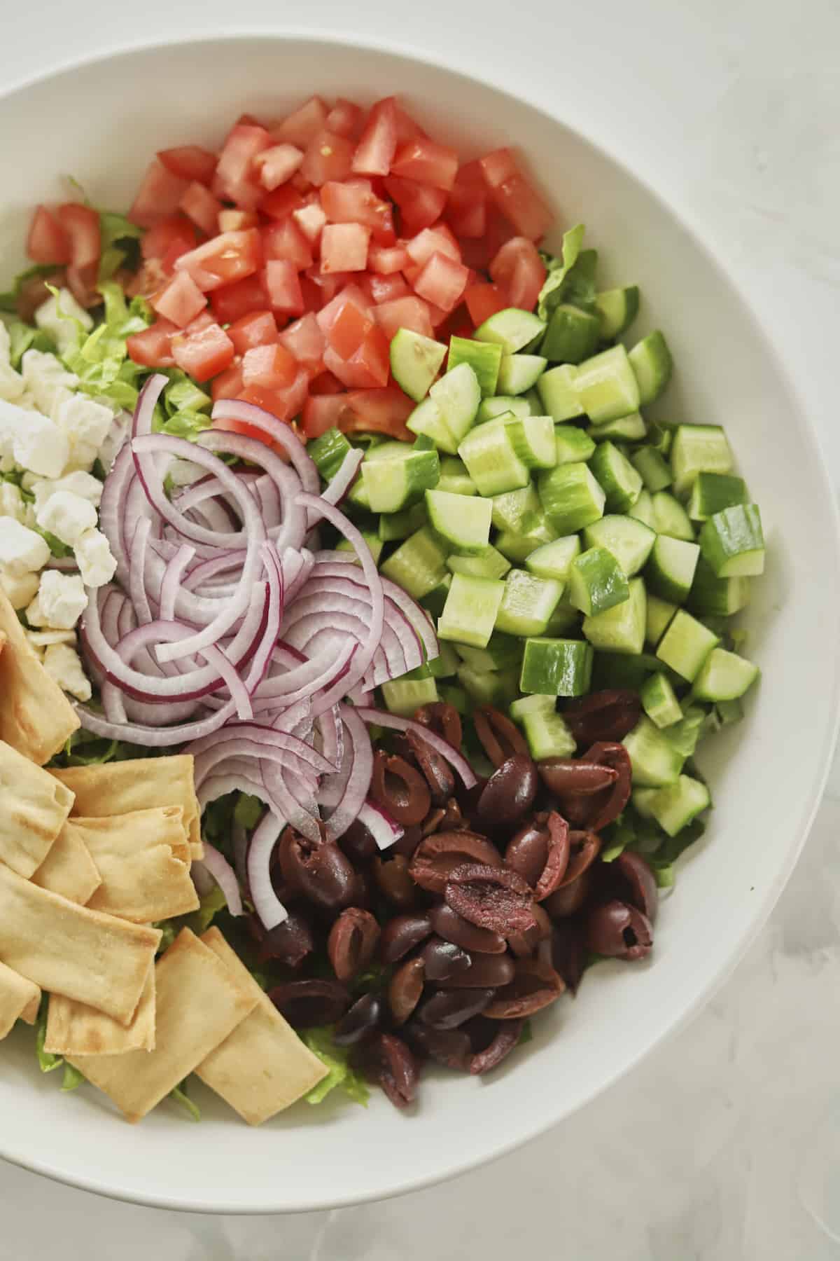 overhead image of an unmixed Greek salad in a white bowl