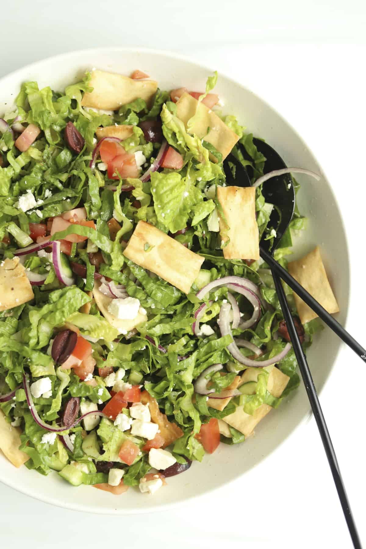 overhead image of Greek salad in a bowl with serving utensils on the side