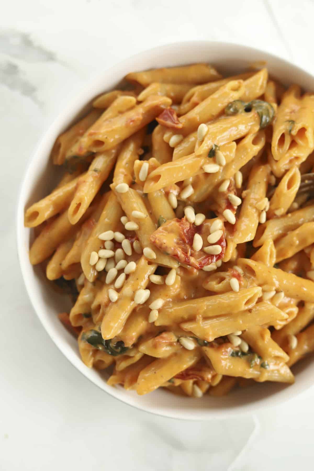 a bowl of one pot sun-dried tomato pasta topped with pine nuts