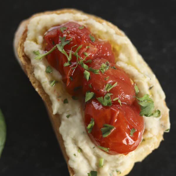 A piece of crostini topped with white bean dip and roasted tomatoes.