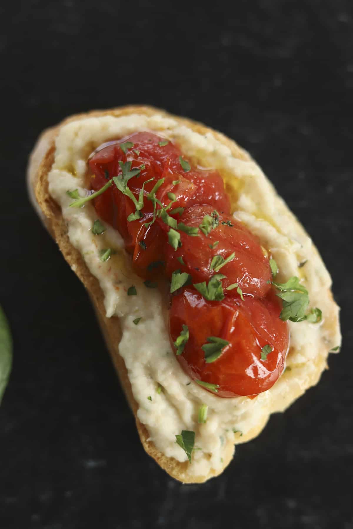 A piece of crostini topped with white bean dip and roasted tomatoes.