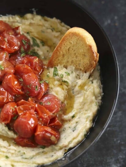 A bowl of white bean dip topped with roasted tomatoes with crostini.